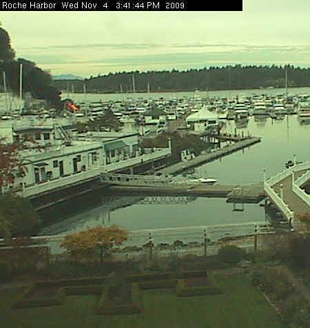 Flames are visible in the upper left part of this image captured by IslandCam.com's Roche Harbor camera. One boat is reported fully engulfed in flames. San Juan Island Fire Department