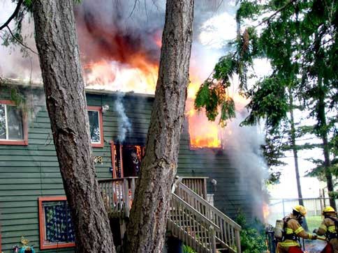 Flames shoot out of the top floor of a Friday Harbor home that was destroyed by a fast-moving fire early Tuesday afternoon. Its five occupants were either not at home when the fire broke or escape without injury.